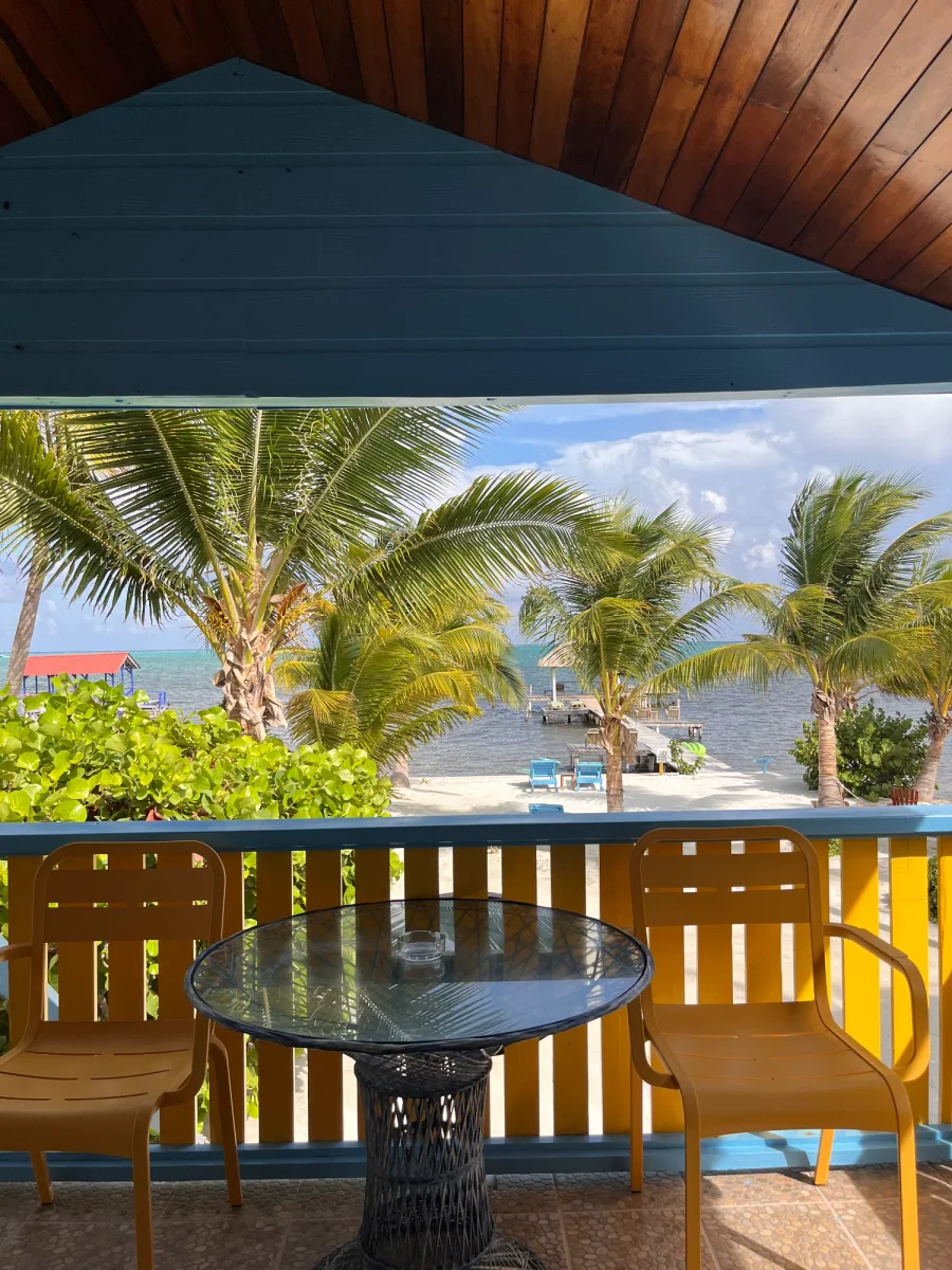 Ocean view from a covered balcony at Colinda Cabanas, with palm trees, the Caribbean Sea, and the dock in Caye Caulker, Belize