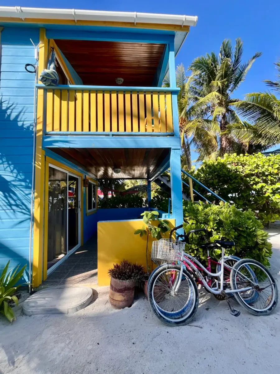 Bright blue and yellow cabana exterior with complimentary bicycles and tropical landscaping at Colinda Cabanas in Caye Caulker, Belize